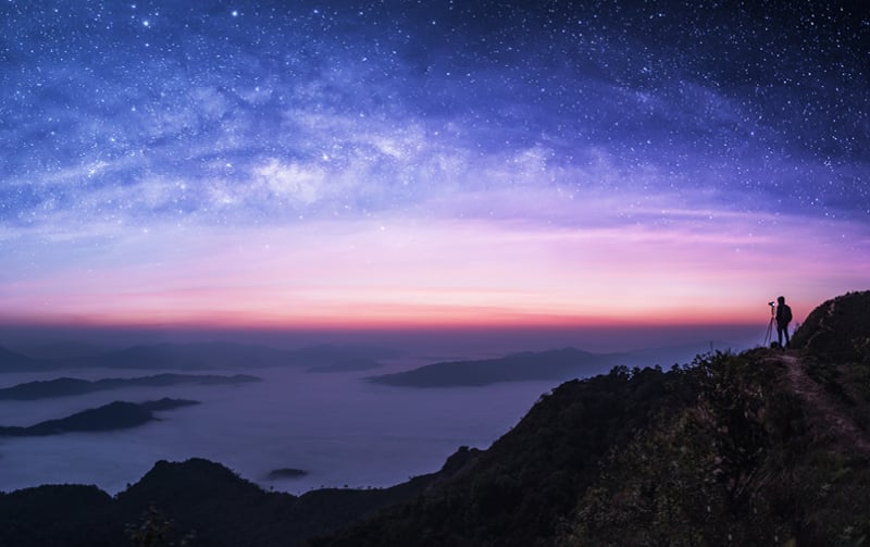 Person standing in the distance with camera overlooking a starry sky